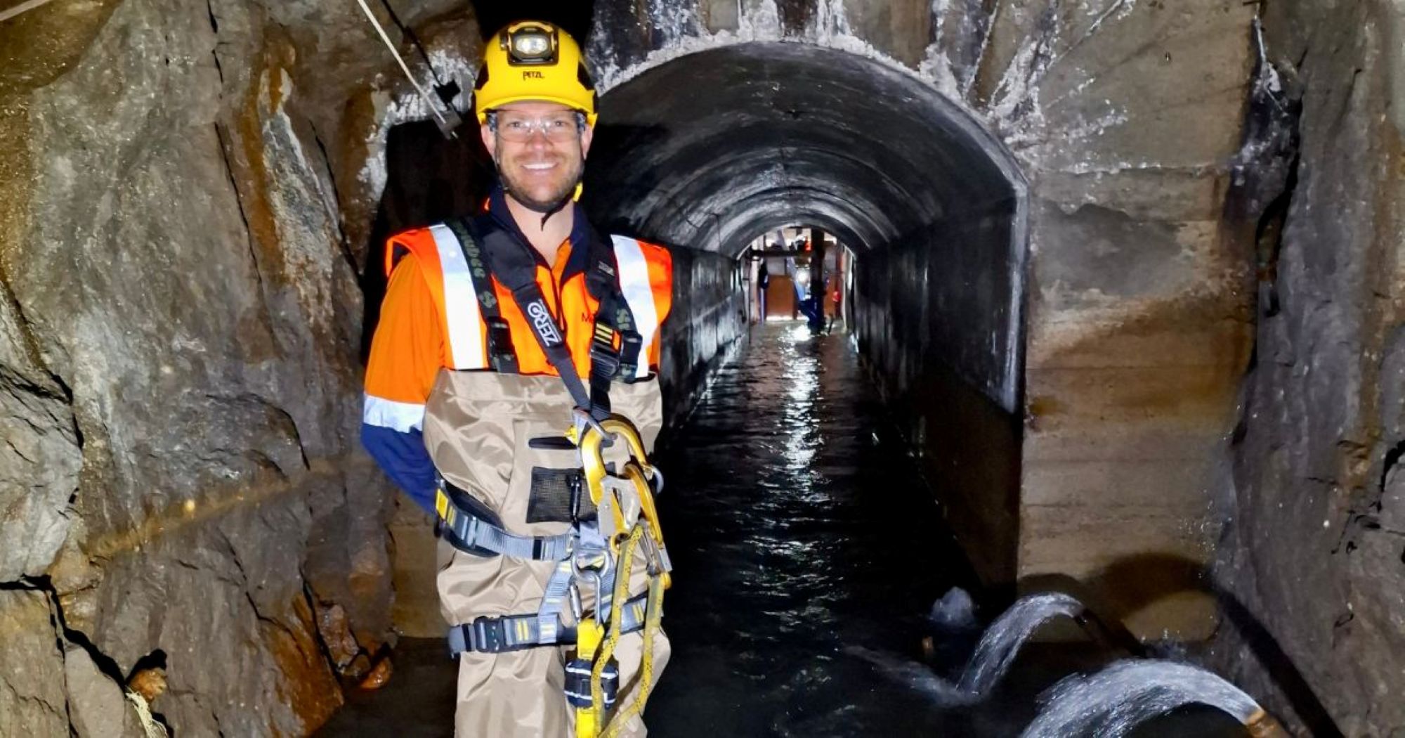 Man in PPE and wearing a harness stood inside a tunnel with water on the floor