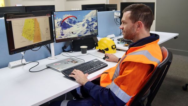 Man in orange hi-viz seated at desk operating a computer with two screens.