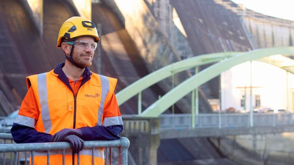 Man in PPE standing with hydro power dam spillway in background