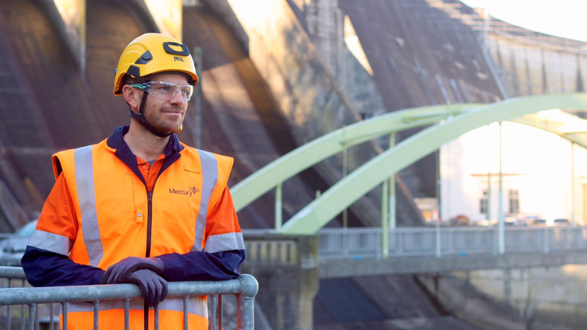 Man in PPE standing with hydro power dam spillway in background