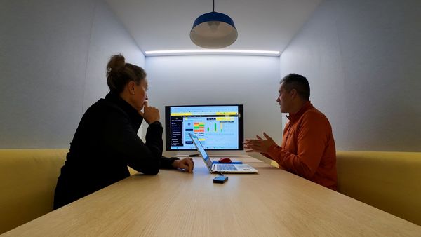Two people sat in a collaboration booth in an office looking at a shared screen, with a laptop on the table between them.