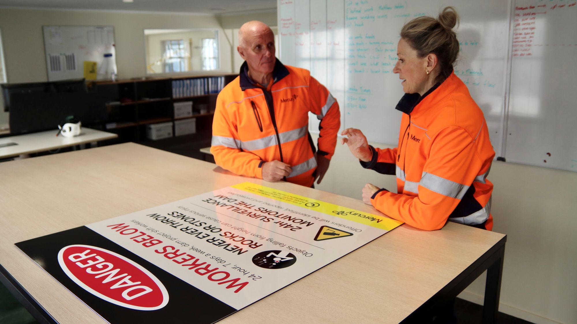 Two people talking with a hazard sign on the table in front of them