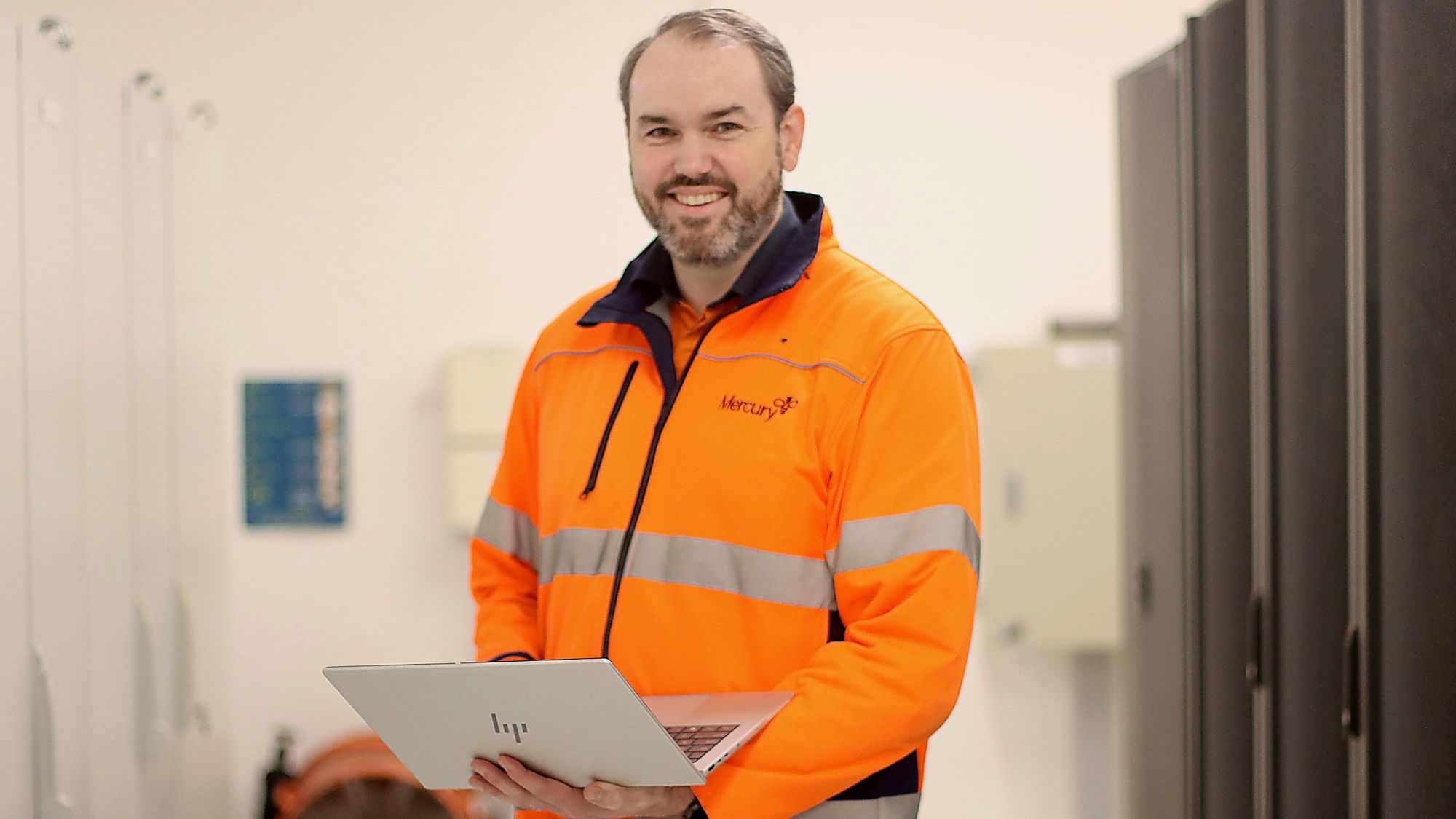 Man in hi-viz Mercury branded jacket holding a laptop