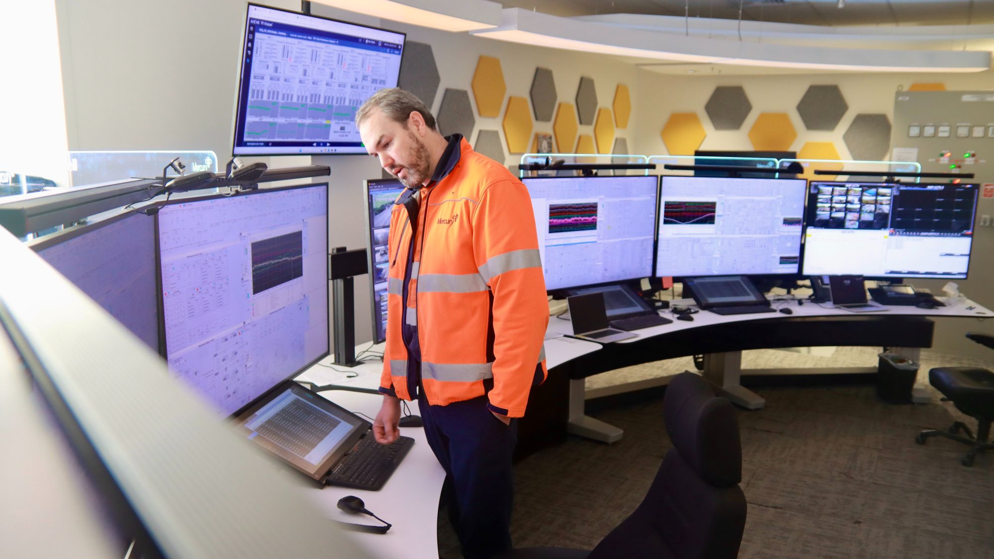 Man in orange hi-viz jacket standing at a control room desk