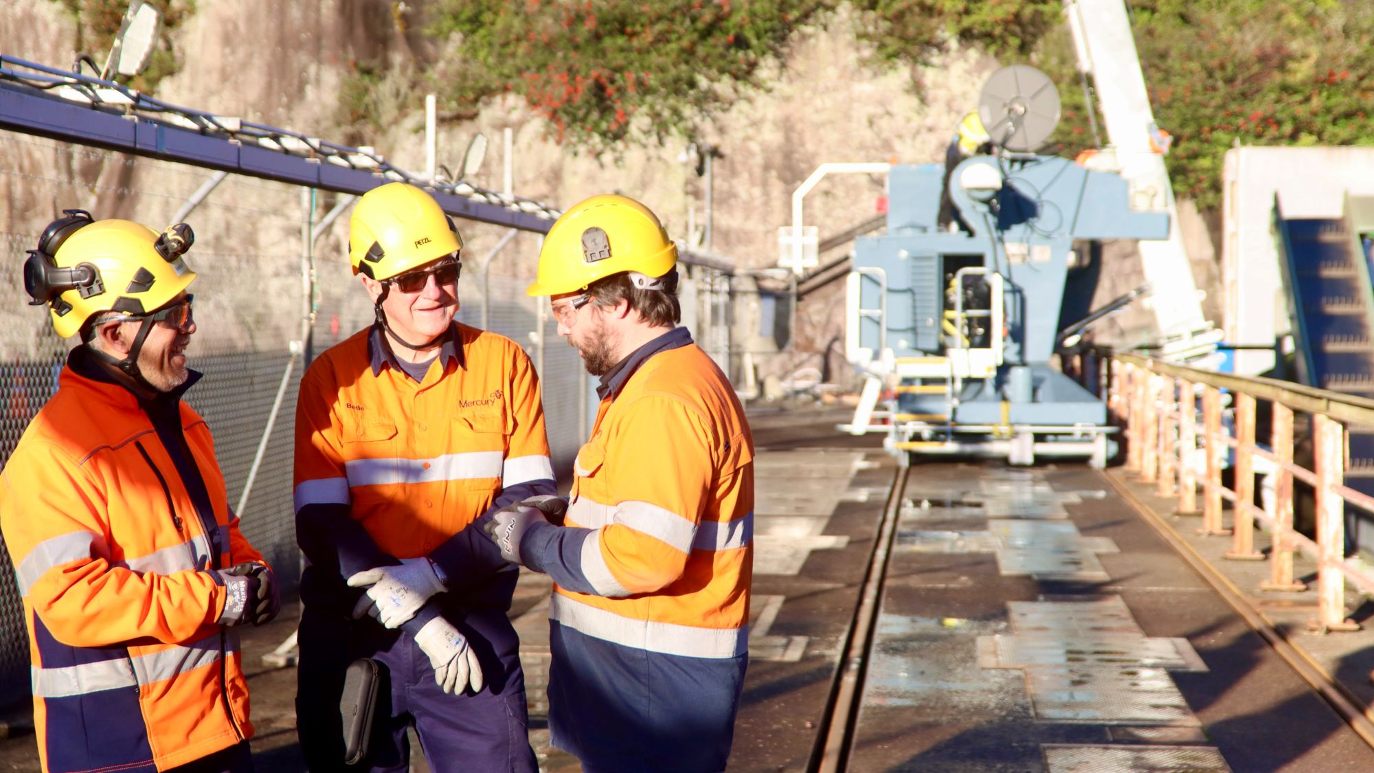 three men in PPE on dam with screen cleaning machine in background