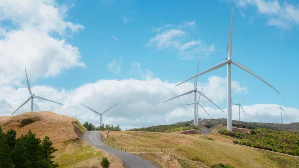 road heading over brow of hill with wind-turbines on horizon